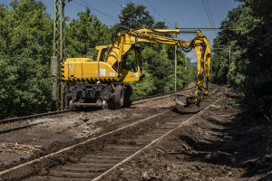 Kotrógép dolgozik a vasúti pálya hordaléktól való megtisztításán.